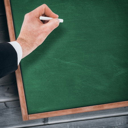 Hand of businessman writing with a white chalk against blackboard with copy space on wooden boardの写真素材
