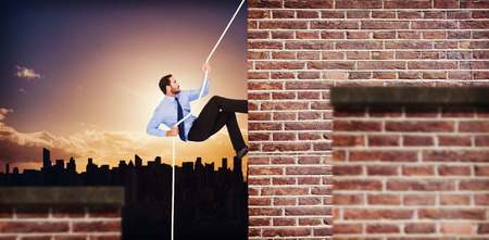 Businessman pulling a rope with effort against red brick wallの写真素材