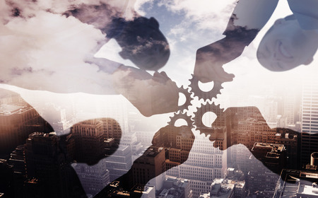 Business colleagues holding cog against aerial view of a city on a cloudy dayの写真素材