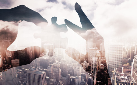 hands holding jigsaw against aerial view of a city on a cloudy dayの写真素材