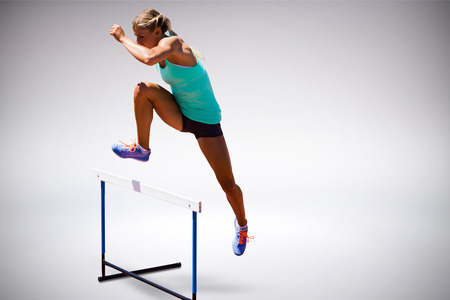 Athlete woman jumping a hurdle against grey backgroundの写真素材