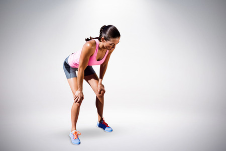 Athletic woman resting with hands on knees against grey background