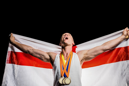 Athlete with gold medals around his neck posing with england flag after victory on black backgroundの写真素材