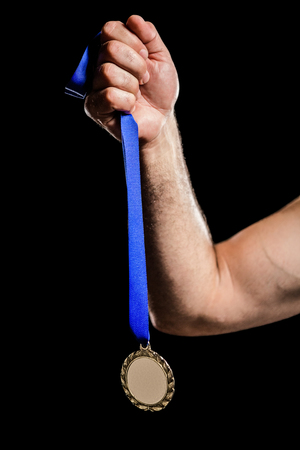 Hand holding a gold medal against black backgroundの写真素材