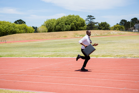 Businessman with briefcase running on a running trackの写真素材