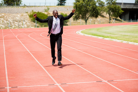 Excited businessman standing on the running track with hands raisedの写真素材