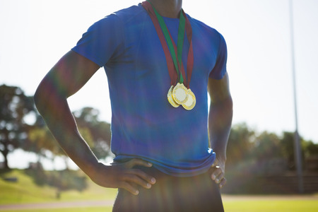 Mid section of athlete posing with gold medal after victory on running trackの写真素材