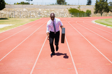 Businessman with briefcase running on a running trackの写真素材