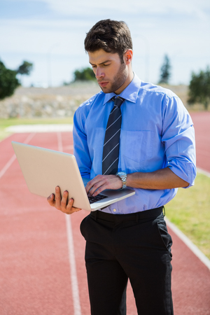 Businessman standing on a running track and using a laptopの写真素材