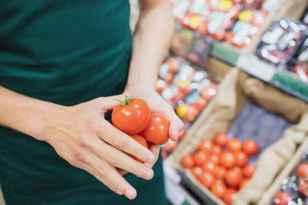 Focus on foreground of man grocer holding tomatoes on a groceryの写真素材