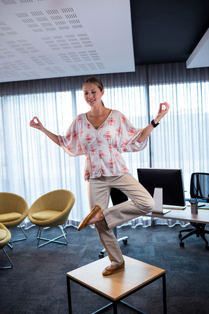 Businesswoman doing yoga on a table in the officeの写真素材