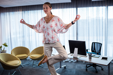 Businesswoman doing yoga on a table in the officeの写真素材