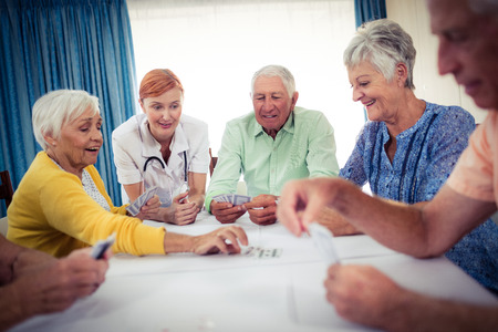 Pensioners playing cards with nurse in the retirement houseの写真素材