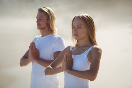 Man and woman performing yoga on beachの写真素材
