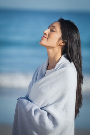 Young woman wrapped in towel standing on beachの写真素材