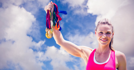 Portrait of happy sportswoman raising her medals  against blue sky with white cloudsの写真素材