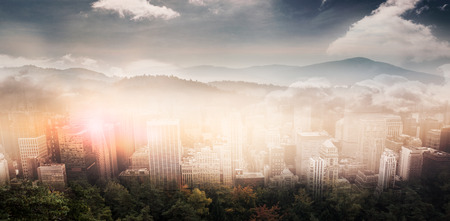 Trees and mountain range against cloudy sky against aerial view of a city on a cloudy dayの写真素材
