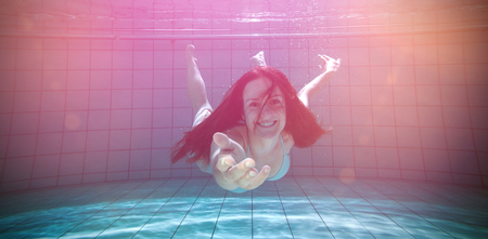 Pretty brunette smiling and offering her hand underwater in the swimming pool at the leisure centreの写真素材