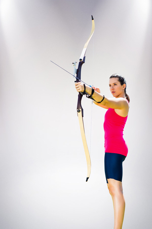 Sportswoman practicing archery on a white background against grey backgroundの写真素材
