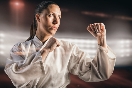 Female fighter performing karate stance against composite image of playing field indoorの写真素材