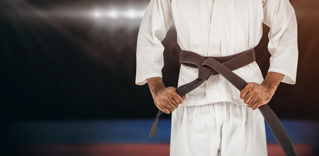 Fighter tightening karate belt against composite image of playing field indoorの写真素材