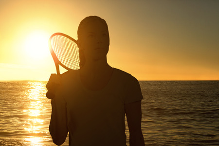 Female tennis player posing with racket against sunset of a beautiful dayの写真素材