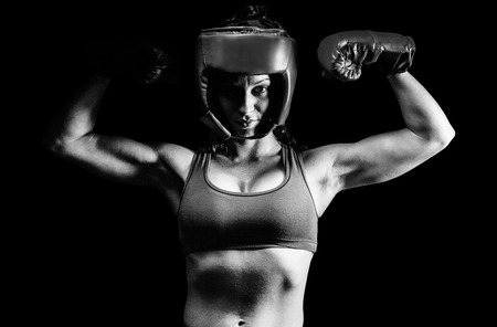 Portrait of confident female fighter flexing muscles against black backgroundの写真素材