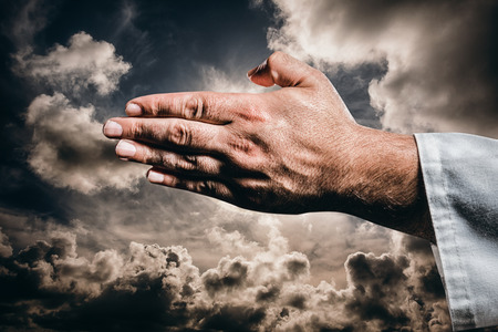 Karate player making hand gesture on black background against dark sky with white cloudsの写真素材