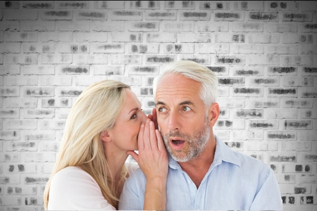 Composite image of woman is telling a secret to a man in front of a bricks wallの写真素材