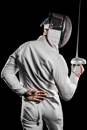 Rear view of man wearing fencing suit practicing with sword on black background
