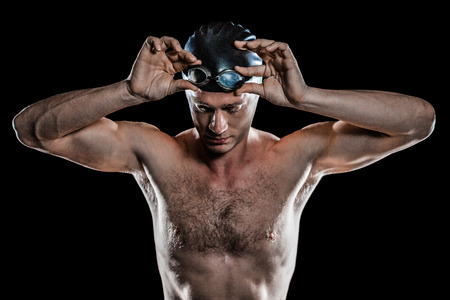 Swimmer looking down and holding swimming goggles on black backgroundの写真素材
