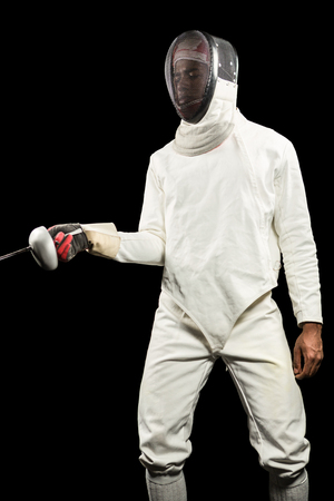 Man wearing fencing suit practicing with sword on black background