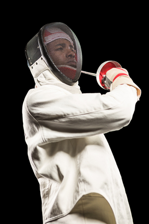 Man wearing fencing suit practicing with sword on black background