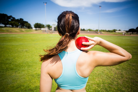 Rear view of female athlete preparing to throw shot put ball in stadiumの写真素材