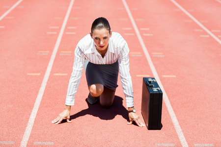 Businesswoman with briefcase in ready to run position on running trackの写真素材