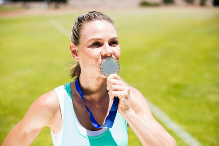 Female athlete kissing his gold medal in stadiumの写真素材