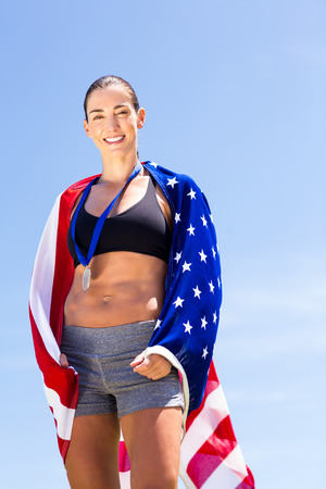 Portrait of female athlete wrapped in american flag in stadiumの写真素材