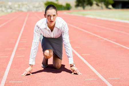 Businesswoman in ready to run position on running track