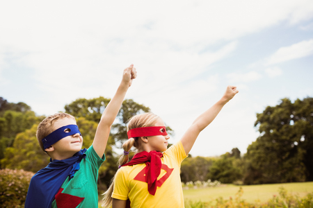 Two cute children pretending to fly in superhero costume in the parkの写真素材