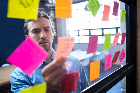 Hipster reading a post it on a window in the office Hipster reading a post it on a window in the office