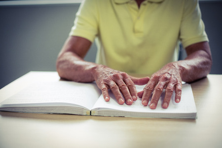Senior blind man reading a braille book at homeの写真素材