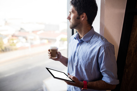 Casual businessman holding a cup of tea and a tablet computer in the officeの写真素材