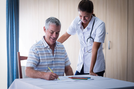 Doctor assisting a senior man while drawing in drawing book at homeの写真素材