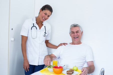 Portrait of senior man and female doctor smiling in hospital while having breakfastの写真素材