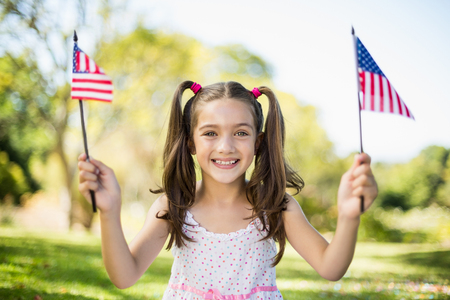 Portrait of cute girl holding American flags in parkの写真素材