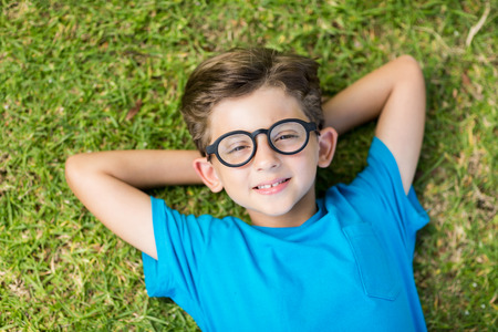 Portrait of young boy in spectacle lying on grass in park