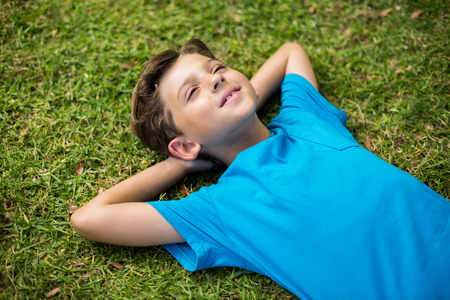 Cute young boy lying on grass in park