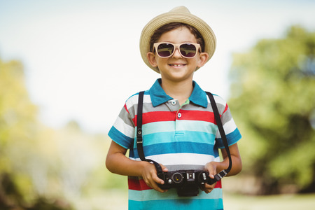 Smiling young boy in sunglasses holding a camera in parkの写真素材