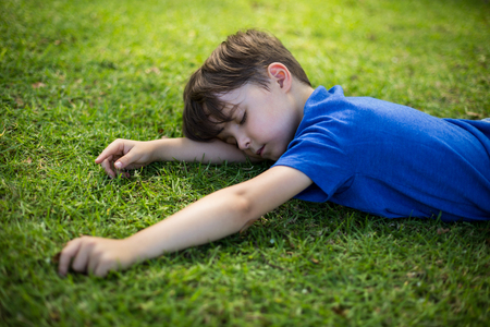 Cute young boy sleeping on grass in parkの写真素材