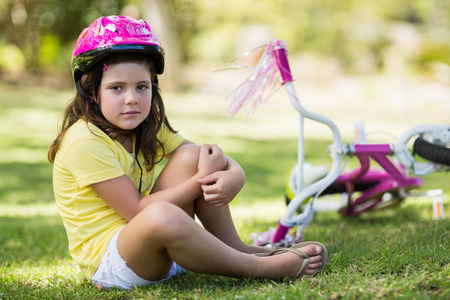 Portrait of young girl getting injured after falling from bicycle in parkの写真素材